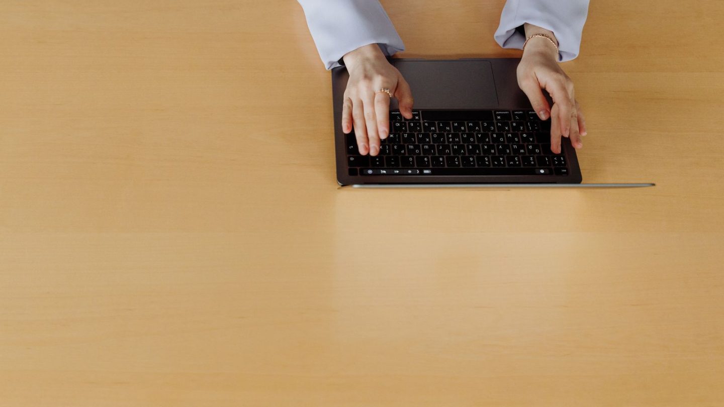 Close-up of hands typing on a laptop keyboard at a desk