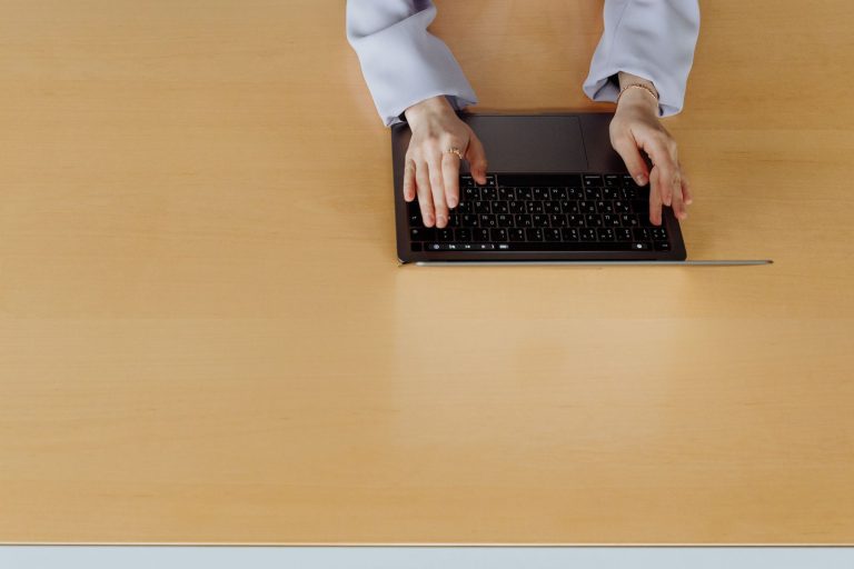 Close-up of hands typing on a laptop keyboard at a desk