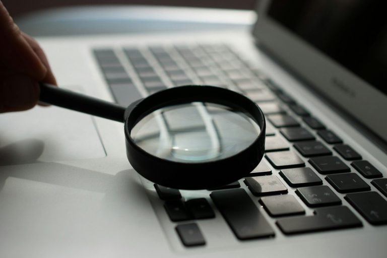 Hand holding a magnifying glass over a laptop keyboard, representing a WordPress speed test