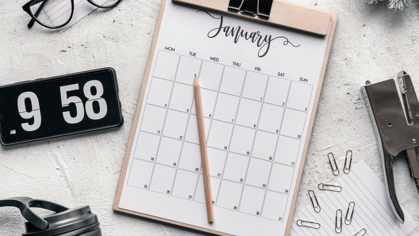 Monthly calendar on a clipboard with a pencil, glasses and stationery on a desk