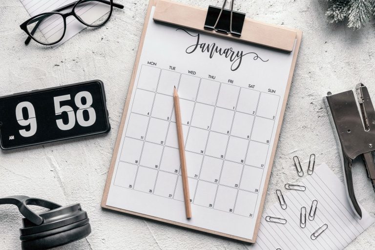 Monthly calendar on a clipboard with a pencil, glasses and stationery on a desk