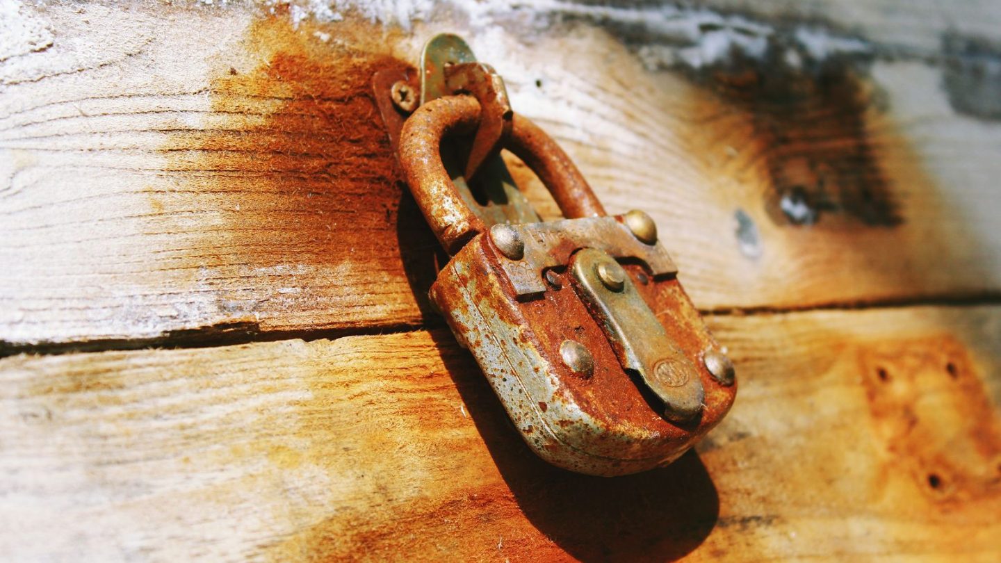 Old rusty padlock hanging on a weathered wooden door