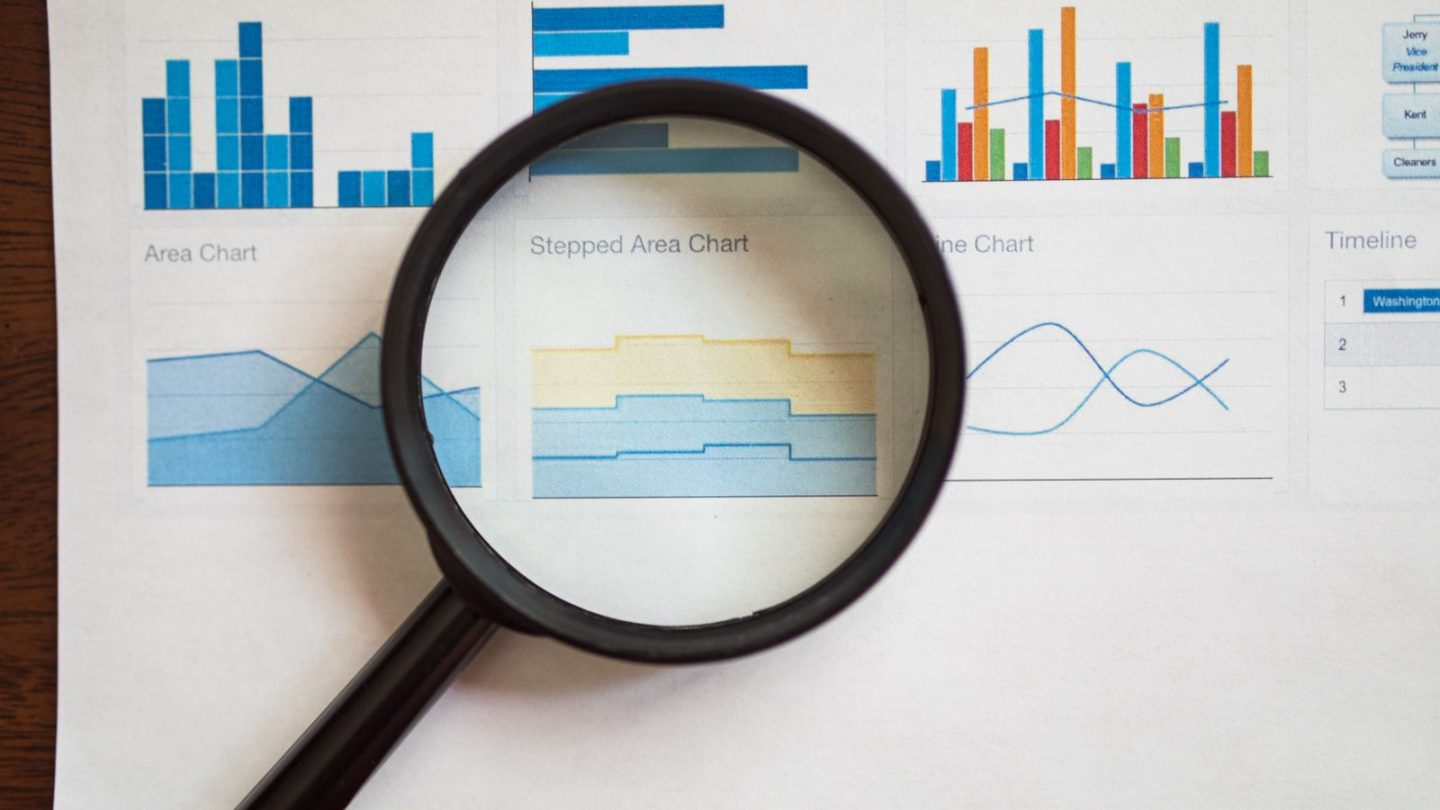 Magnifying glass resting on a printed page of bar, area and line charts
