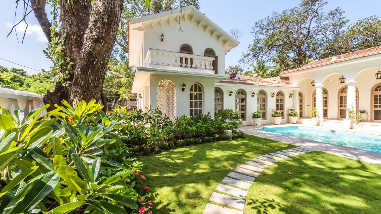 White villa with a swimming pool and tropical garden on a sunny day