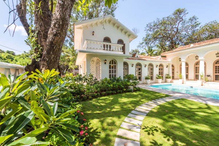 White villa with a swimming pool and tropical garden on a sunny day